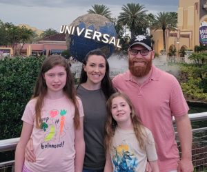 Rachel and her husband with daughters Lydia and Charlotte standing closely together and smiling into the camera at Universal Studios in Florida