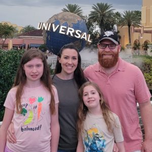 Rachel and her husband with daughters Lydia and Charlotte standing closely together and smiling into the camera at Universal Studios in Florida