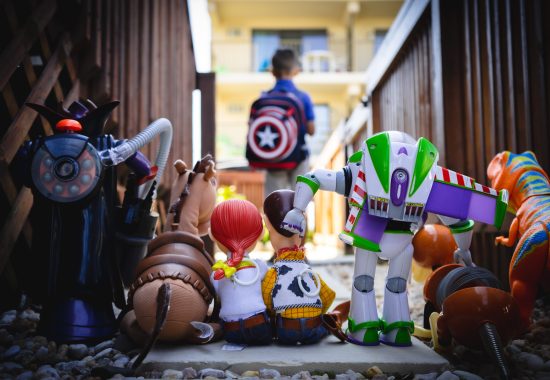 Photo of Toy Story characters facing away from the camera looking toward a young boy with a Captain America backpack on in the background waiting for the school bus