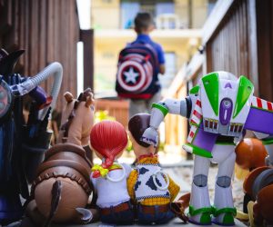 Photo of Toy Story characters facing away from the camera looking toward a young boy with a Captain America backpack on in the background waiting for the school bus