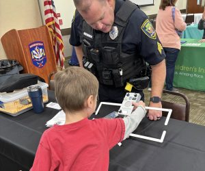 safety expo child police officer demonstrating Project Lifesaver to a child